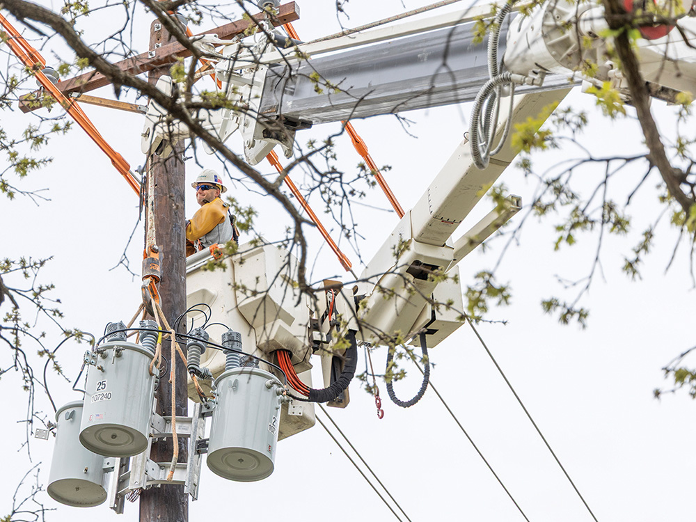 Técnicos de líneas eléctricas instalando un nuevo poste, un transformador y una línea de servicio subterránea.